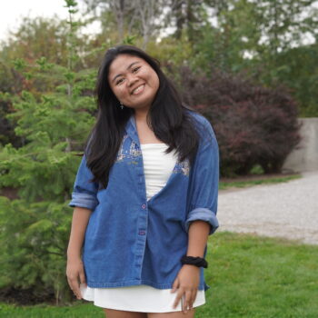 Student in a blue shirt stands in a garden.