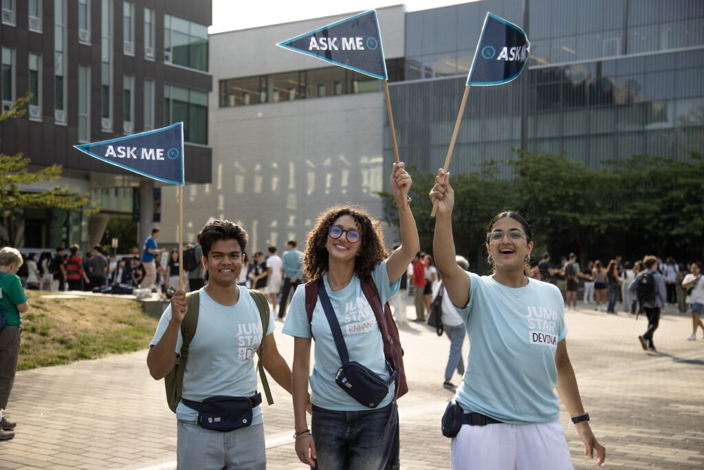 three students smiling and waving mini blue flags at JumpStart event